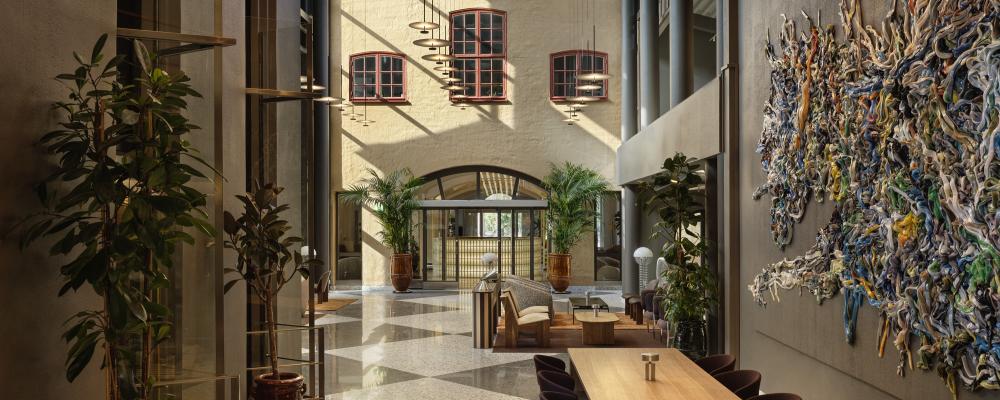 Det stora entréplanet har grafiska rutgolv i svart och vitt, betong, stålkonstruktioner och grå väggar kontrasteras av trämöbler, läder och textilier i chokladbrunt och varma toner.