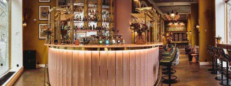 På bilden syns den nya cocktailbaren där väggarna är målade i en vacker senapsgul färg som går i kontrast med de rosa och gröna,
guldiga tonerna som binder ihop rummets detaljrikedom. Foto: Christian Fang