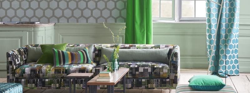 esigners Guild har en rad nya dekorativa, abstrakta mönster. Chandigarh på soffan är en sammetsväv med ett intrikat, grafiskt, digitaltryckt mönster.  Metalltrådar ökar lystern. Gardiner är Calozzo i smaragd och azurblå Zardozi. På schäslongen ett randigt tyg som plockats upp i en kudde. Foto Designers Guild