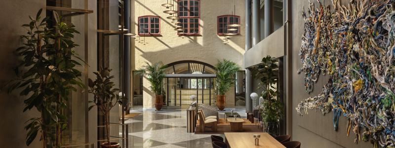 Det stora entréplanet har grafiska rutgolv i svart och vitt, betong, stålkonstruktioner och grå väggar kontrasteras av trämöbler, läder och textilier i chokladbrunt och varma toner.