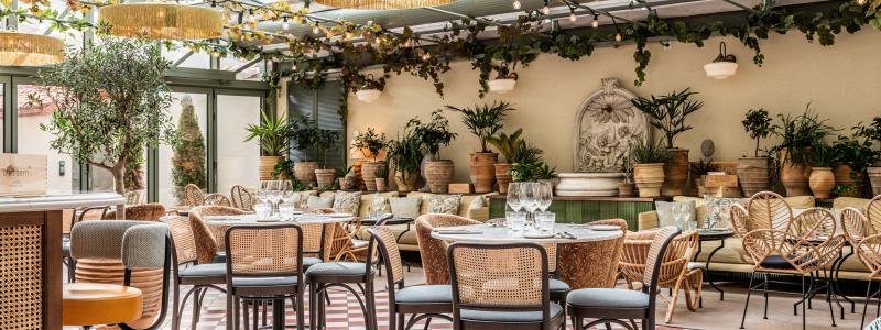 Isolas Ginbar. Ljusfyllt orangeri med glasat tak, terrakottaklinker, fontän och en mix av rotting och klädda stolar i grönskande atmosfär.
Foto: Philip Liljenberg