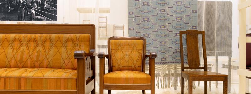 Möbler i jugendstil från verkstädernas tidiga år, kring 1910. Soffan och fåtöljen ritades av NK:s chefsarkitekt David Blomberg och stolen av Carl Westman, för Nyköpings tingshus. Textilier har alltid funnits med i NK:s utställningar och i de uppbyggda miljöerna på varuhuset. Gardinlängden är från Thyra Grafströms textilateljé, för en NK-miljö på Baltiska utställningen i Malmö 1914. Foto: Björn Dahlgren/Sörmlands museum