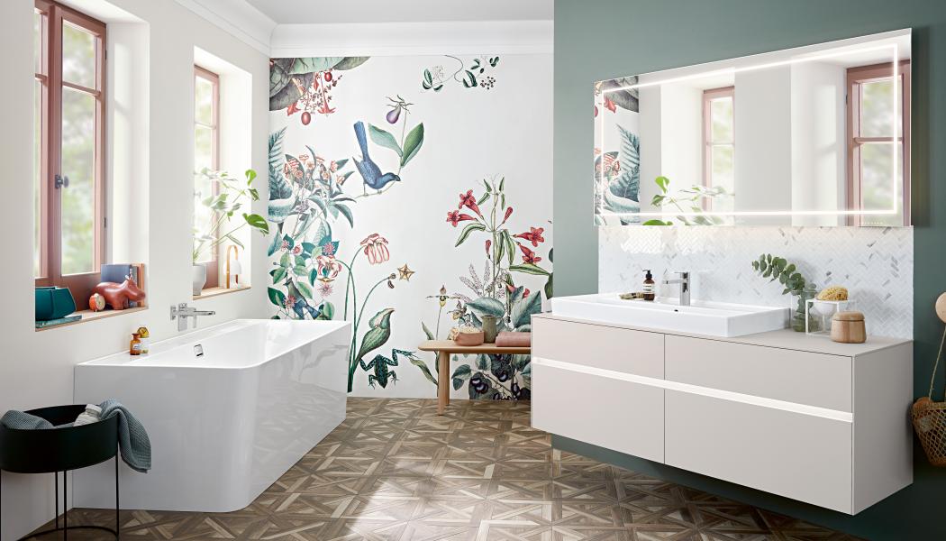 En ljus, ombonad miljö från Villeroy & Boch. Generösa Collaro handfat i TitanCeram finns i många former och storlekar. Badkaret i samma kollektion är i akryl 
och kan fås i andra färger. Skarpa linjer i kritvitt mot den blommiga tapeten ger en fräsch känsla. Foto Villeroy & Boch
