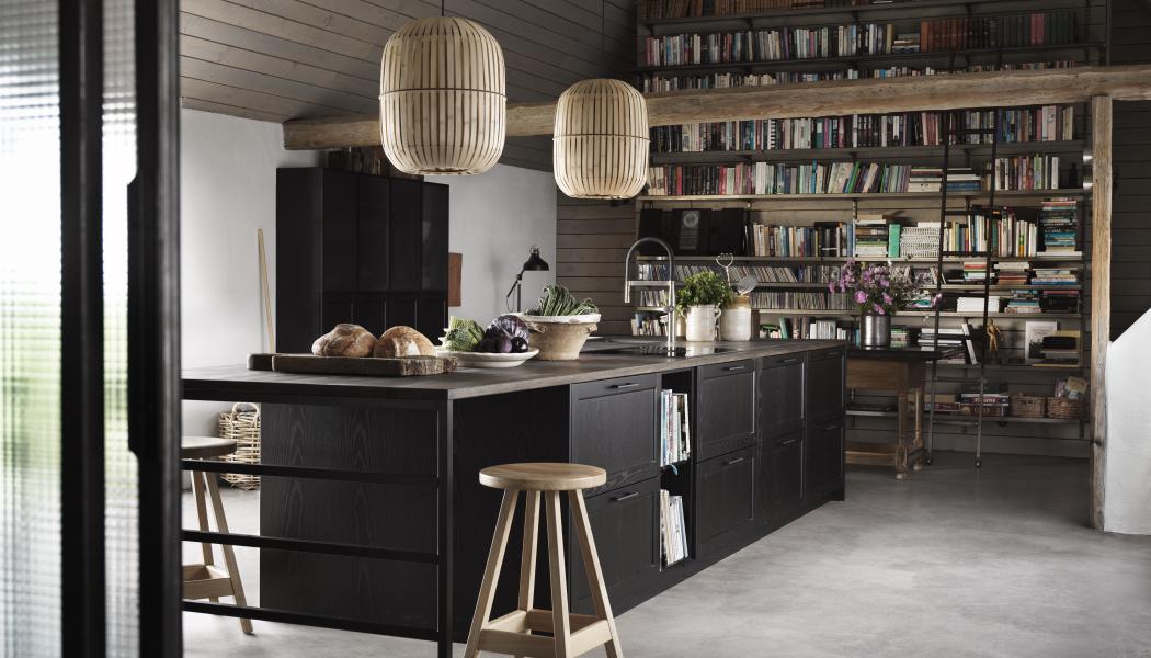 Ett kök att umgås i är svartbetsade Gastro från Ballingslöv. Luckor, lådor och bänkskiva i massiv ek. Den stora köksön rymmer alla kökets funktioner plus smart, luftig matplats. Trivsamt med böcker på väggen och tufft golv i slipad betong. Foto Ballingslöv
