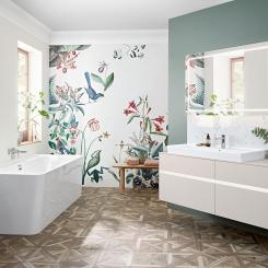 En ljus, ombonad miljö från Villeroy & Boch. Generösa Collaro handfat i TitanCeram finns i många former och storlekar. Badkaret i samma kollektion är i akryl 
och kan fås i andra färger. Skarpa linjer i kritvitt mot den blommiga tapeten ger en fräsch känsla. Foto Villeroy & Boch