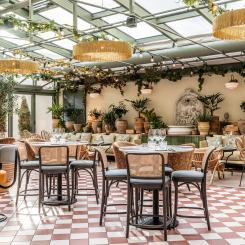 Isolas Ginbar. Ljusfyllt orangeri med glasat tak, terrakottaklinker, fontän och en mix av rotting och klädda stolar i grönskande atmosfär.
Foto: Philip Liljenberg